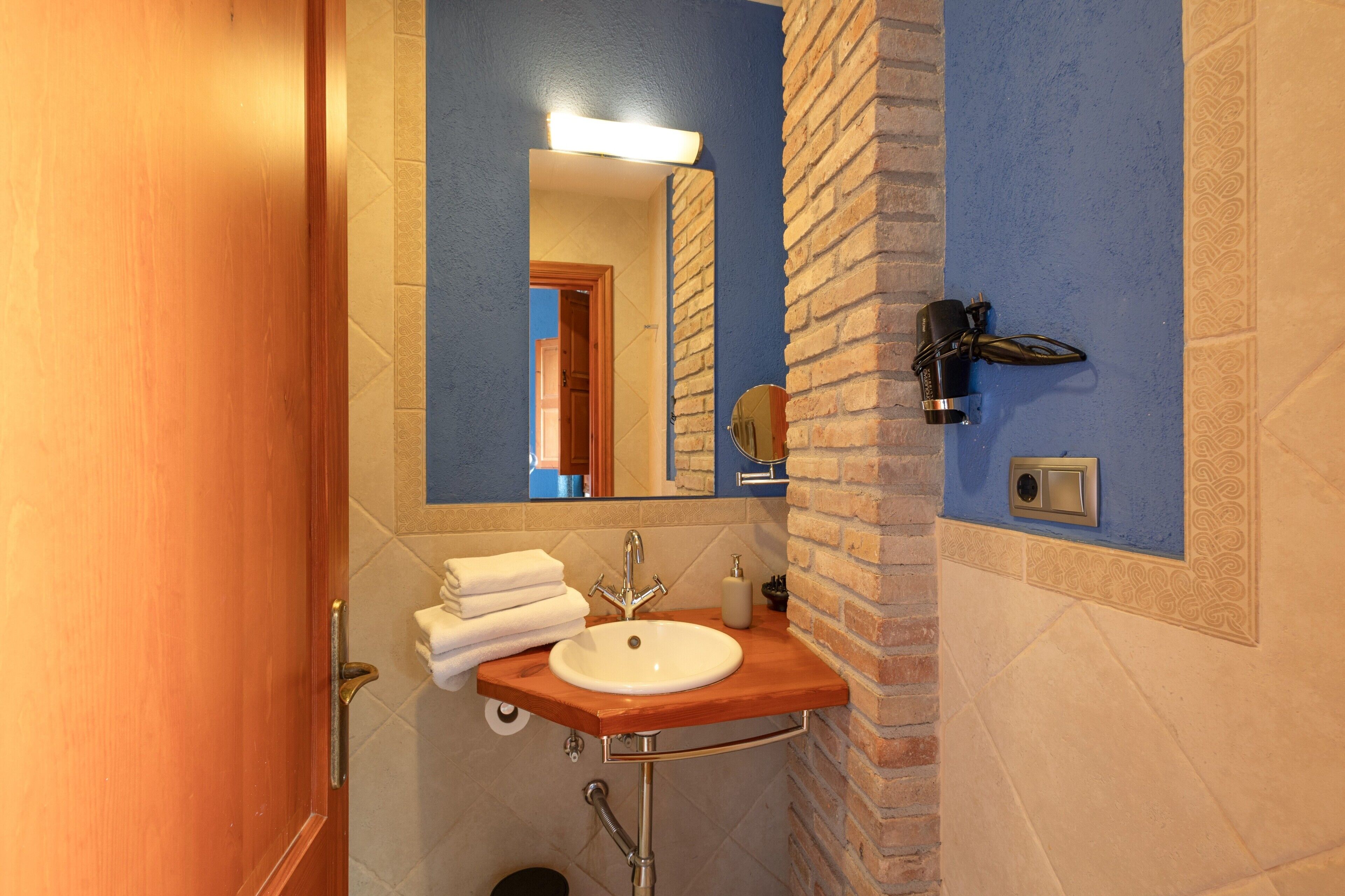 Un baño con un tocador de madera, un lavamanos, un espejo, un perchero para toallas y un secador de pelo montado en la pared.