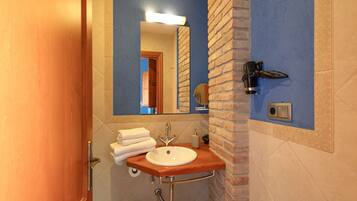 Un baño con un tocador de madera, un lavamanos, un espejo, un perchero para toallas y un secador de pelo montado en la pared.