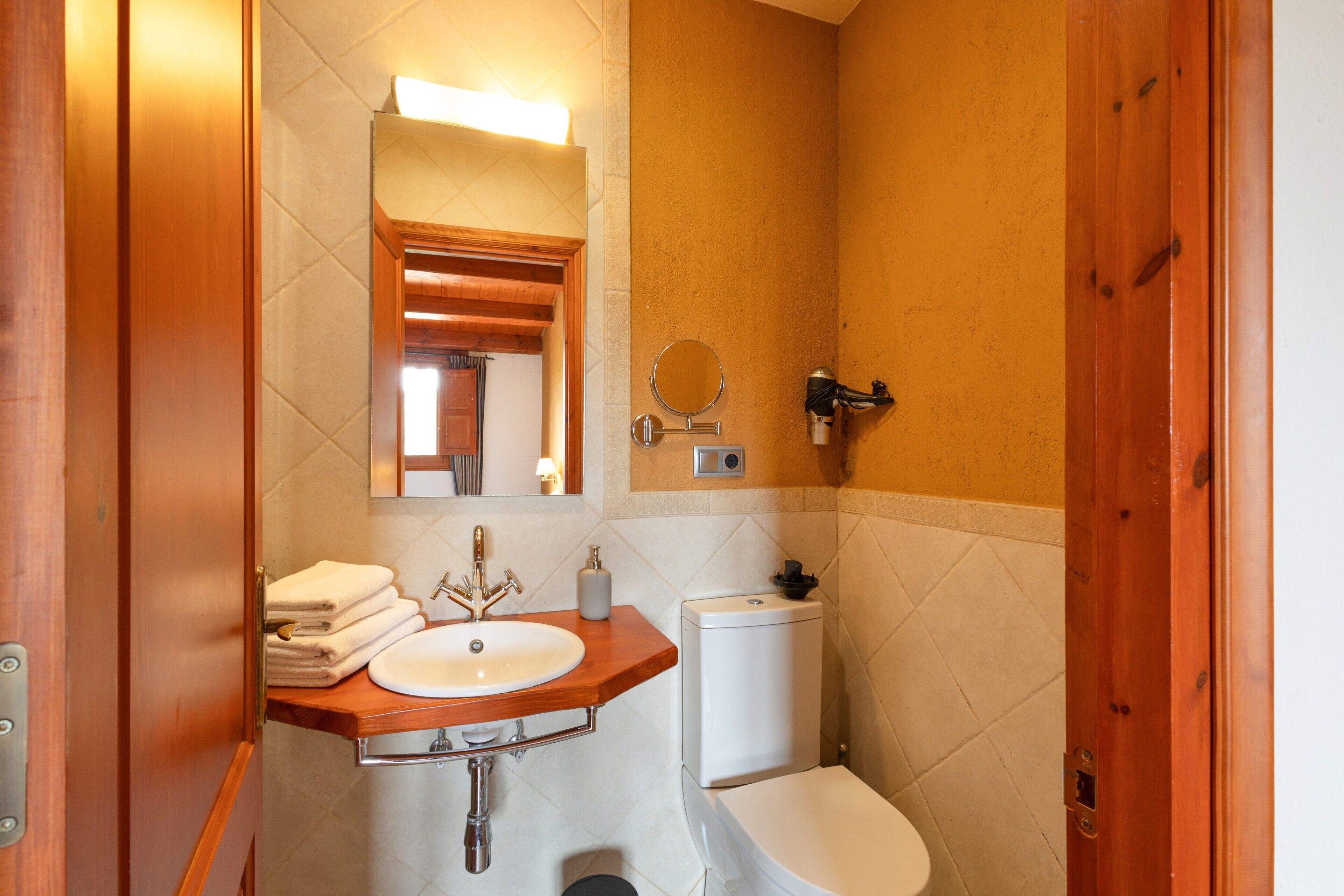 Un baño con tocador de madera, lavamanos, inodoro y espejo.