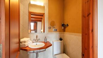 Un baño con tocador de madera, lavamanos, inodoro y espejo.