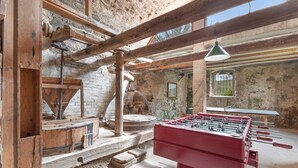 Una habitación con mesa de fútbol, vigas de madera, paredes de piedra y ventana con vistas.