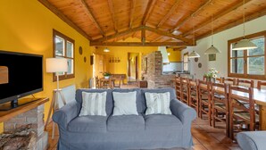 Una sala de estar con un sofá gris, una mesa de comedor de madera y sillas, un televisor y una chimenea.