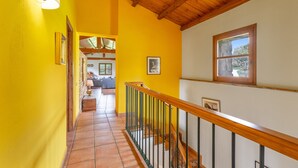 Una escalera con barandillas de madera, paredes amarillas y vista hacia un salón con sofá y ventana.