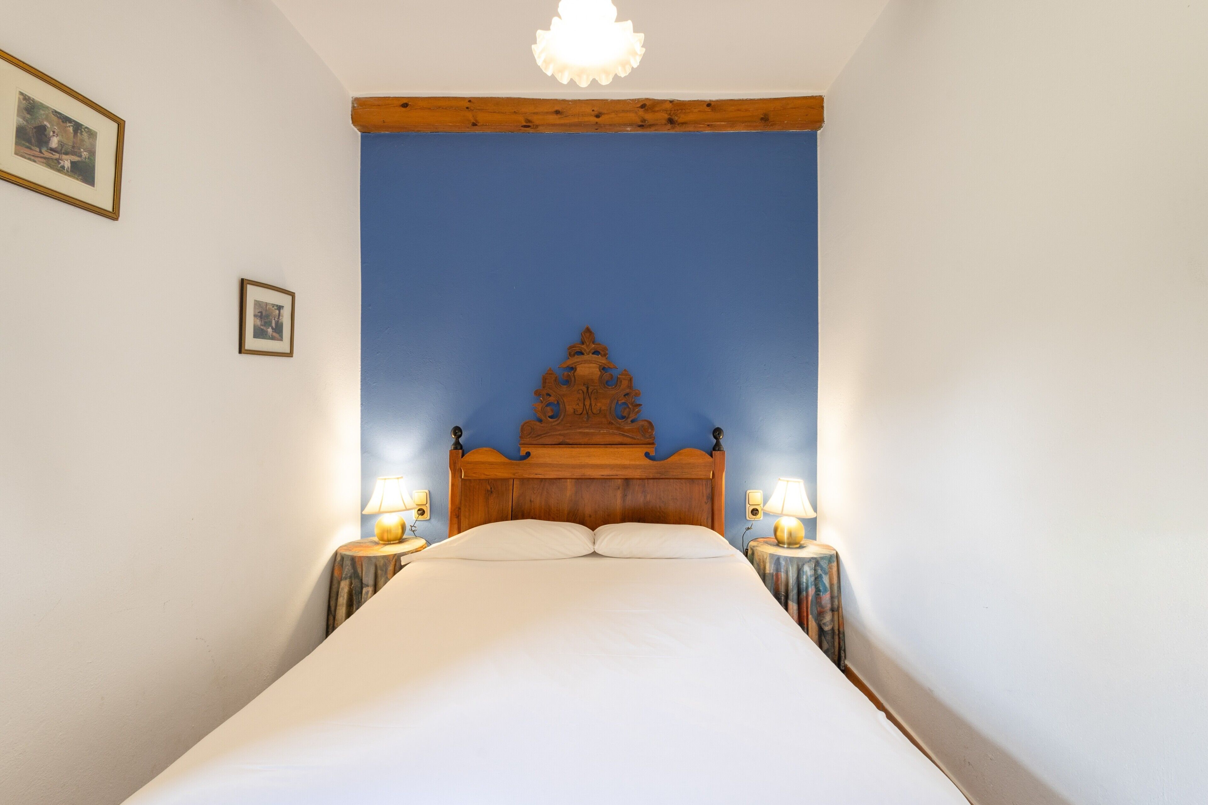 Un dormitorio con cabecera de madera, dos lámparas de noche, una cama con ropa de cama blanca y una pared de acento azul.