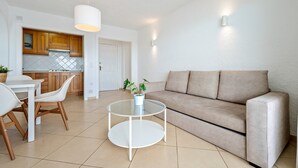Una sala de estar moderna con un sofá color crema, una mesa de centro de vidrio y un comedor con una mesa y sillas blancas.