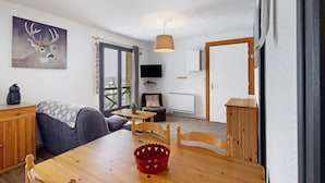 A room with a wooden dining table, chairs, a sofa, a television, and a window with curtains. - Apartment 'Capcir' with Mountain View, Shared Terrace and Wi-Fi (Les Angles)
