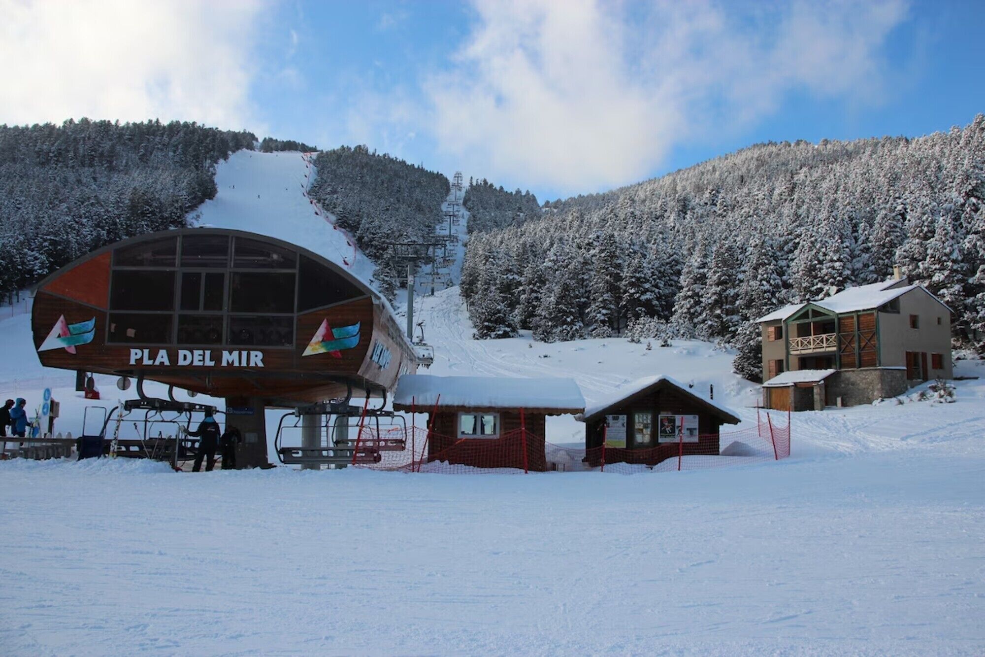 Ein Skigebiet mit Seilbahn, einem Holzhaus mit der Aufschrift 'PLA DEL MIR' und einer kleinen Berghütte.