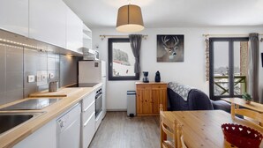 A modern kitchen with a wooden countertop, stainless steel appliances, a dining area with a wooden table and chairs, and a window with a view of a snowy landscape. - Apartment 'Capcir' with Mountain View, Shared Terrace and Wi-Fi (Les Angles)