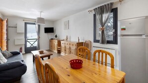 A compact living space with a dining area, kitchenette, and a TV mounted on the wall. - Apartment 'Cerdagne' with Mountain View, Shared Terrace and Wi-Fi (Les Angles)