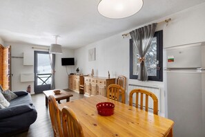 A compact living space with a dining area, kitchenette, and a TV mounted on the wall. - Apartment 'Cerdagne' with Mountain View, Shared Terrace and Wi-Fi (Les Angles)