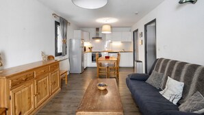 A compact living space with a sofa, wooden dining table, and a kitchenette. - Apartment 'Cerdagne' with Mountain View, Shared Terrace and Wi-Fi (Les Angles)