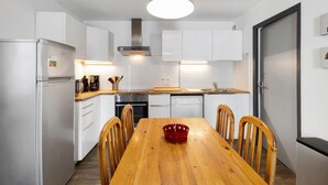 A modern kitchen with white cabinets, stainless steel appliances, a wooden dining table, and a red decorative bowl. - Apartment 'Cerdagne' with Mountain View, Shared Terrace and Wi-Fi (Les Angles)