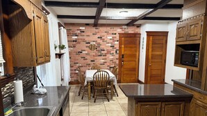 Una cocina con pared de ladrillo, armarios de madera, una mesa de comedor con sillas, un microondas y un lavabo.