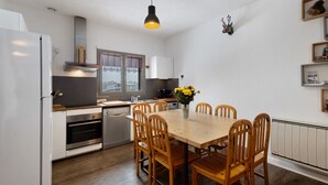 A modern kitchen with a dining table, chairs, a refrigerator, oven, and a window with a view.