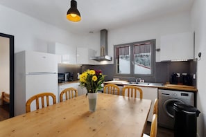 A compact kitchen with a dining table, chairs, a washing machine, and a window with a view of trees. - Apartment 'Roussillon' with Mountain View, Private Terrace and Wi-Fi (Les Angles)