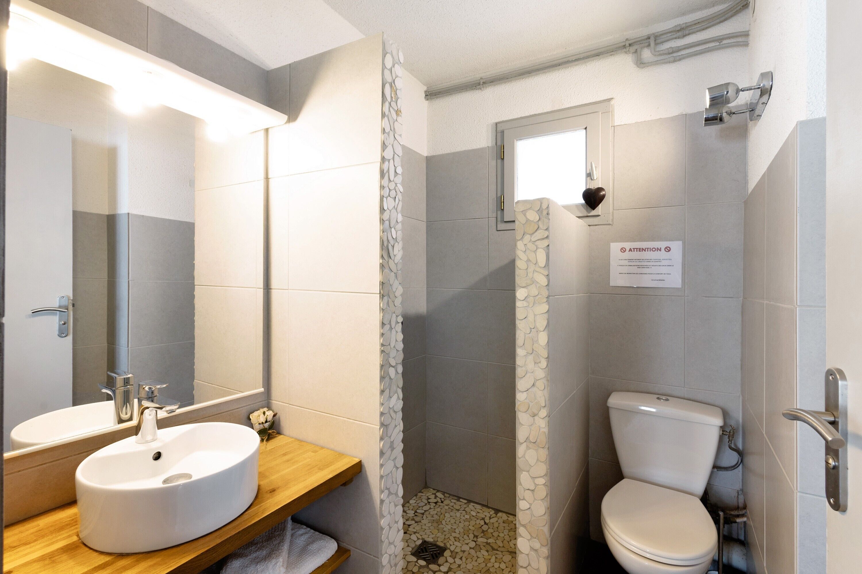 Baño con lavamanos, espejo, inodoro, ducha y señal de precaución.