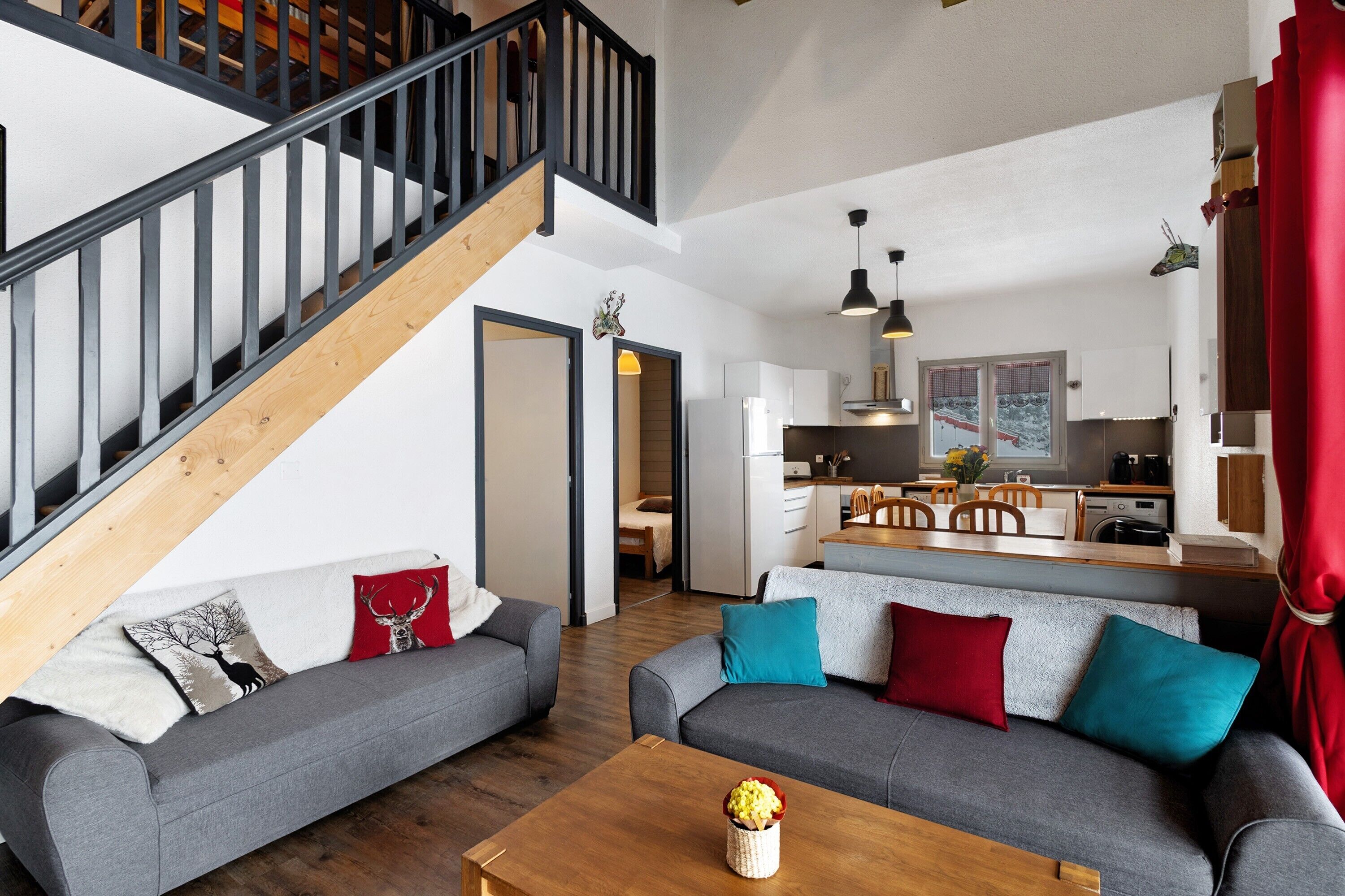 A modern living room with a staircase, grey sofas, a wooden coffee table, and a kitchen in the background.