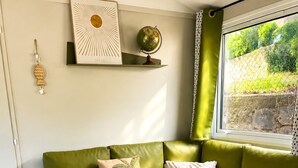 Een moderne woonkamer met een groene bank, een klein bijzettafeltje met een schaal fruit, een wereldbol op een plank en een raam met uitzicht op groen.