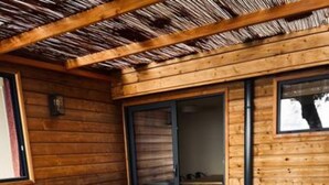 Een modern interieur met een houten plafond, een grijze bank, een houten salontafel en een groot raam.