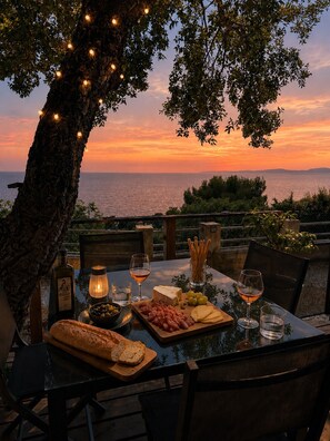 An outdoor dining table set with food and drinks, overlooking a scenic view of the sea at sunset. - Bungalow 'Sunset Lodge' with Sea View, Shared Pool and Air Conditioning (Saint-Raphaël)