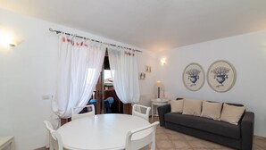 Ein Wohnzimmer mit rundem Tisch, zwei Stühlen, einem Sofa und einem Fenster mit Vorhängen.