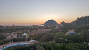Ein Wohngebiet mit Swimmingpool, Liegestühlen und Blick auf das Meer bei Sonnenuntergang.