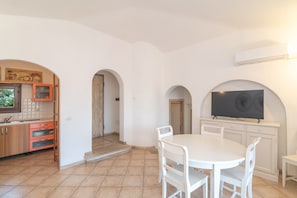 Una cocina amplia con armarios blancos, un comedor con mesa y sillas blancas, y un televisor montado sobre los armarios.