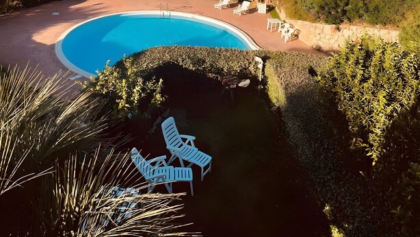 Ein Pool mit Liegestühlen, Bergen im Hintergrund und einer Küstenstadt.
