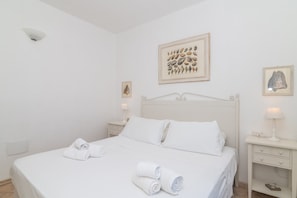 Habitación de hotel blanca con cama, dos mesitas de noche y decoración en la pared.