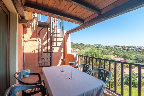 A balcony with a table and chairs, a spiral staircase, and a view of a green landscape.
