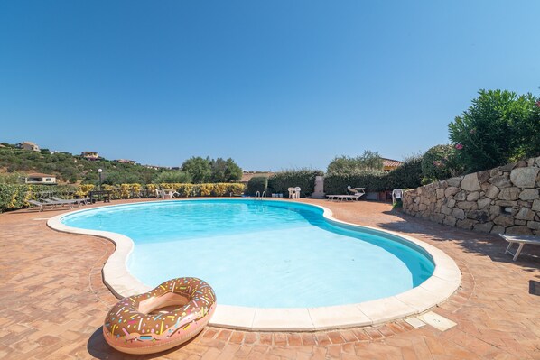 Una piscina con un flotador en forma de rosquilla, rodeada por un muro de piedra y un área de patio con sillas.