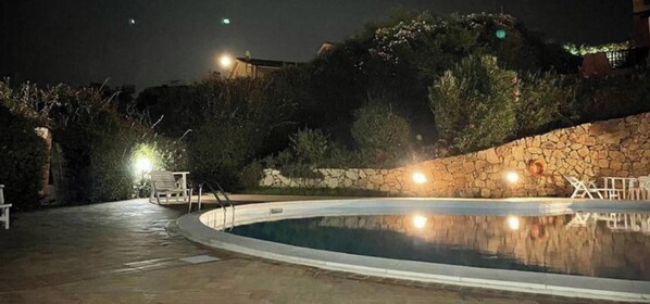 A swimming pool with a stone wall, a chair, and a lamp post.