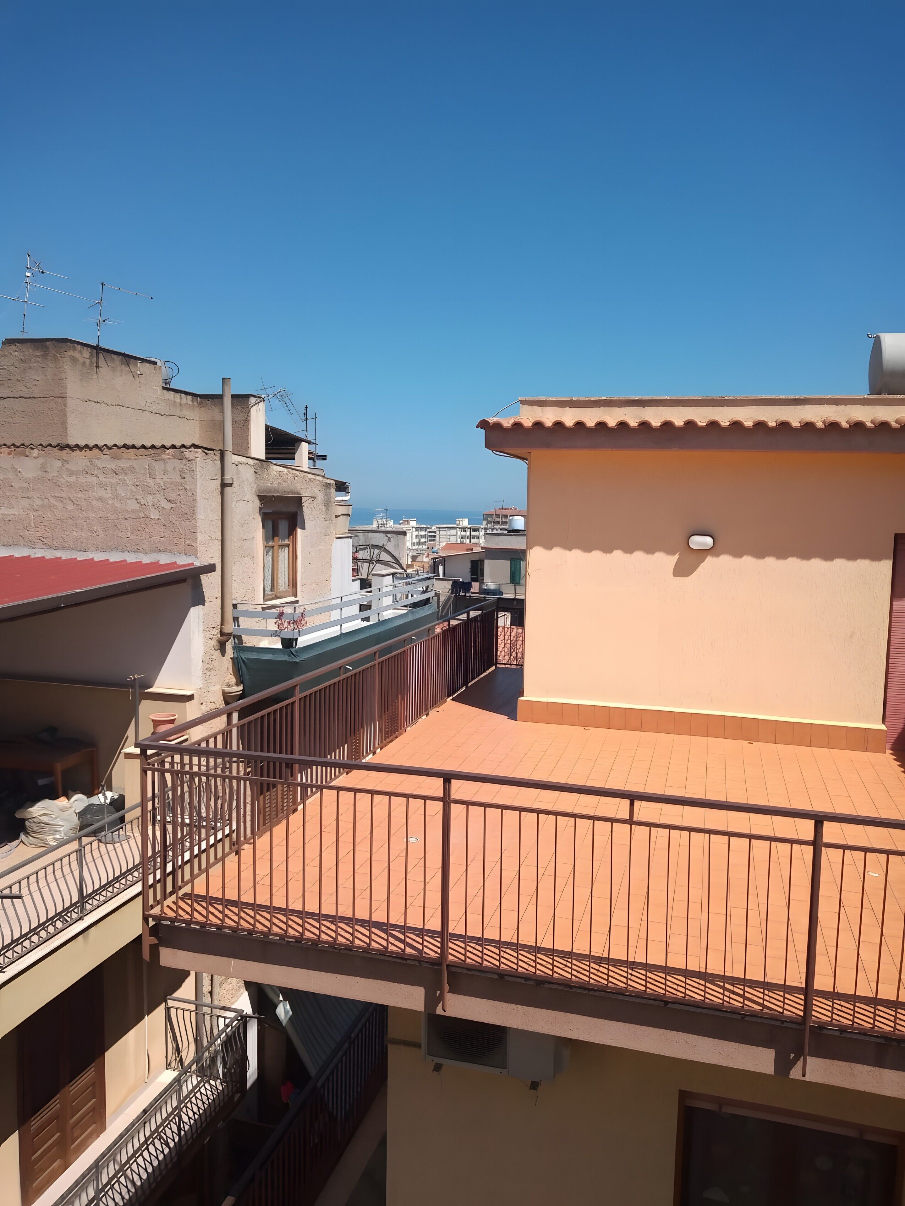 Un edificio residencial con tejado de tejas, balcones con barandillas de metal y una vista despejada al mar.