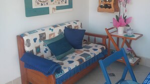 Um quarto aconchegante com um sofá de madeira, uma mesa pequena, uma planta pendurada e uma prateleira fixada na parede.