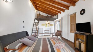 Una camera da letto con un letto, una televisione, un soffitto in legno, una scala e vista su un balcone.