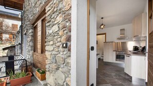 Facciata in pietra con persiane in legno, un balcone con piante in vaso e una cucina moderna con mobili bianchi ed elettrodomestici in acciaio inossidabile.