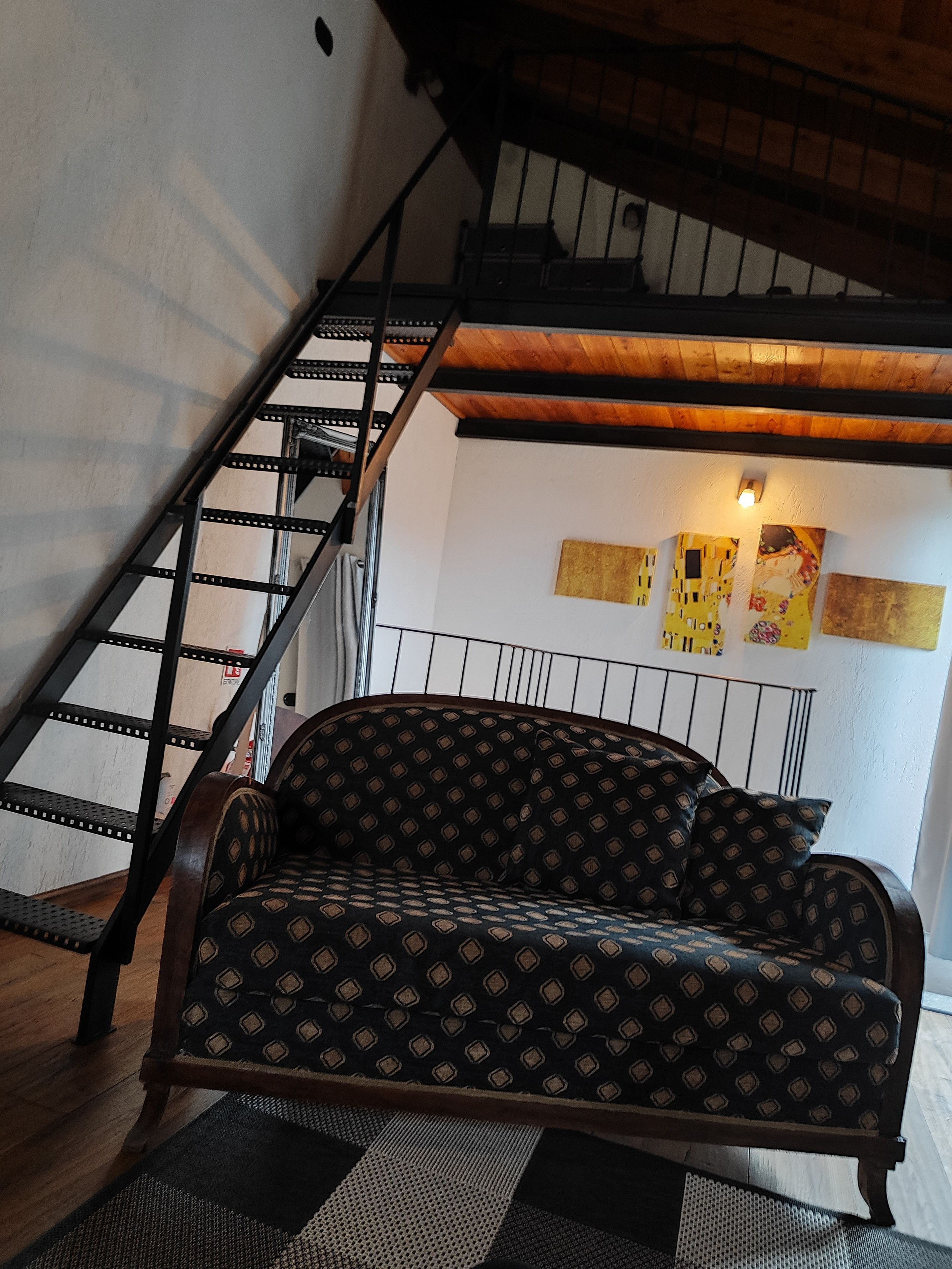 Una habitación con un sofá estampado, una escalera y obras de arte en la pared.