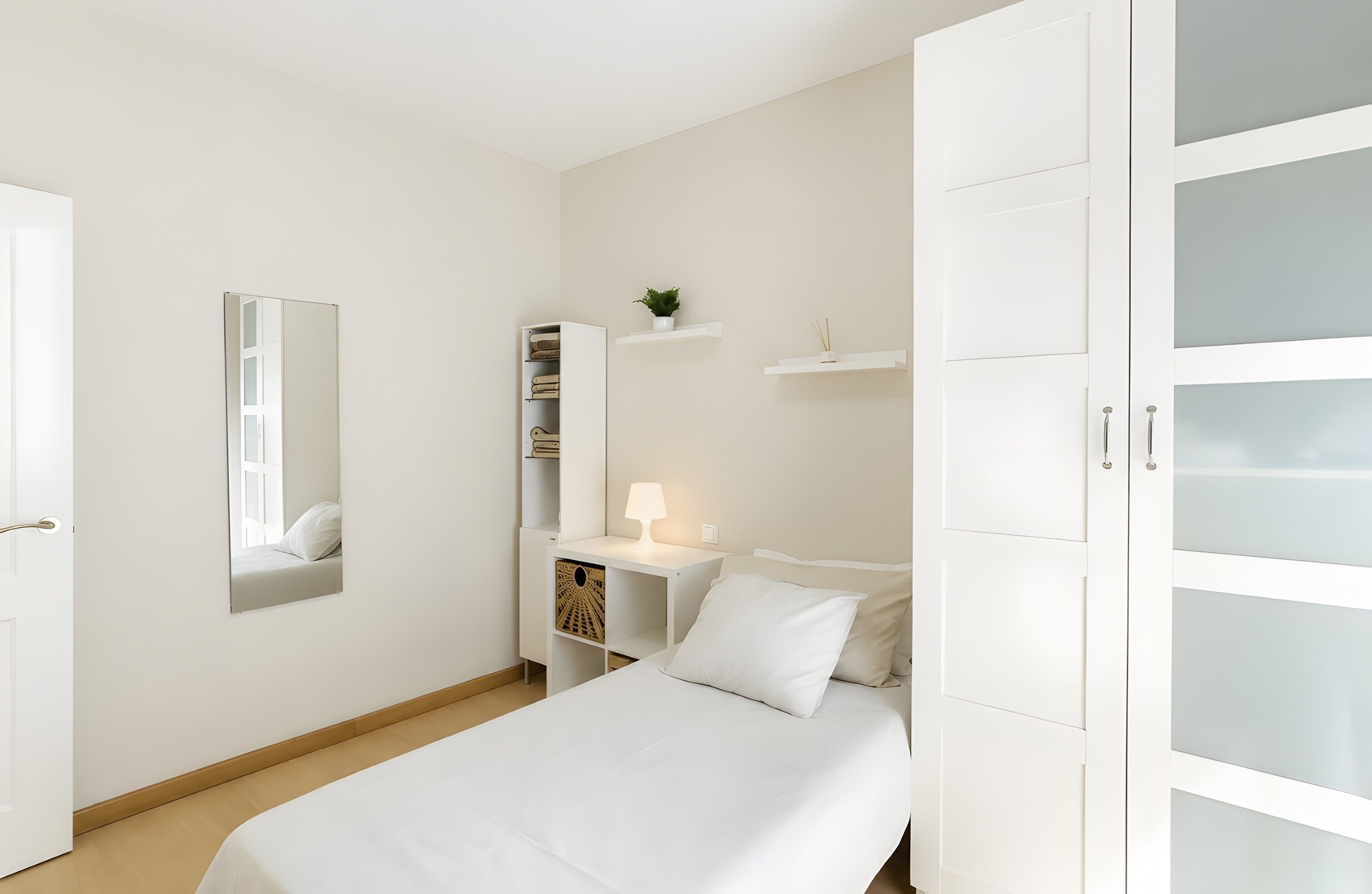 Un dormitorio con cama, una mesita de noche con lámpara, un armario y un espejo.