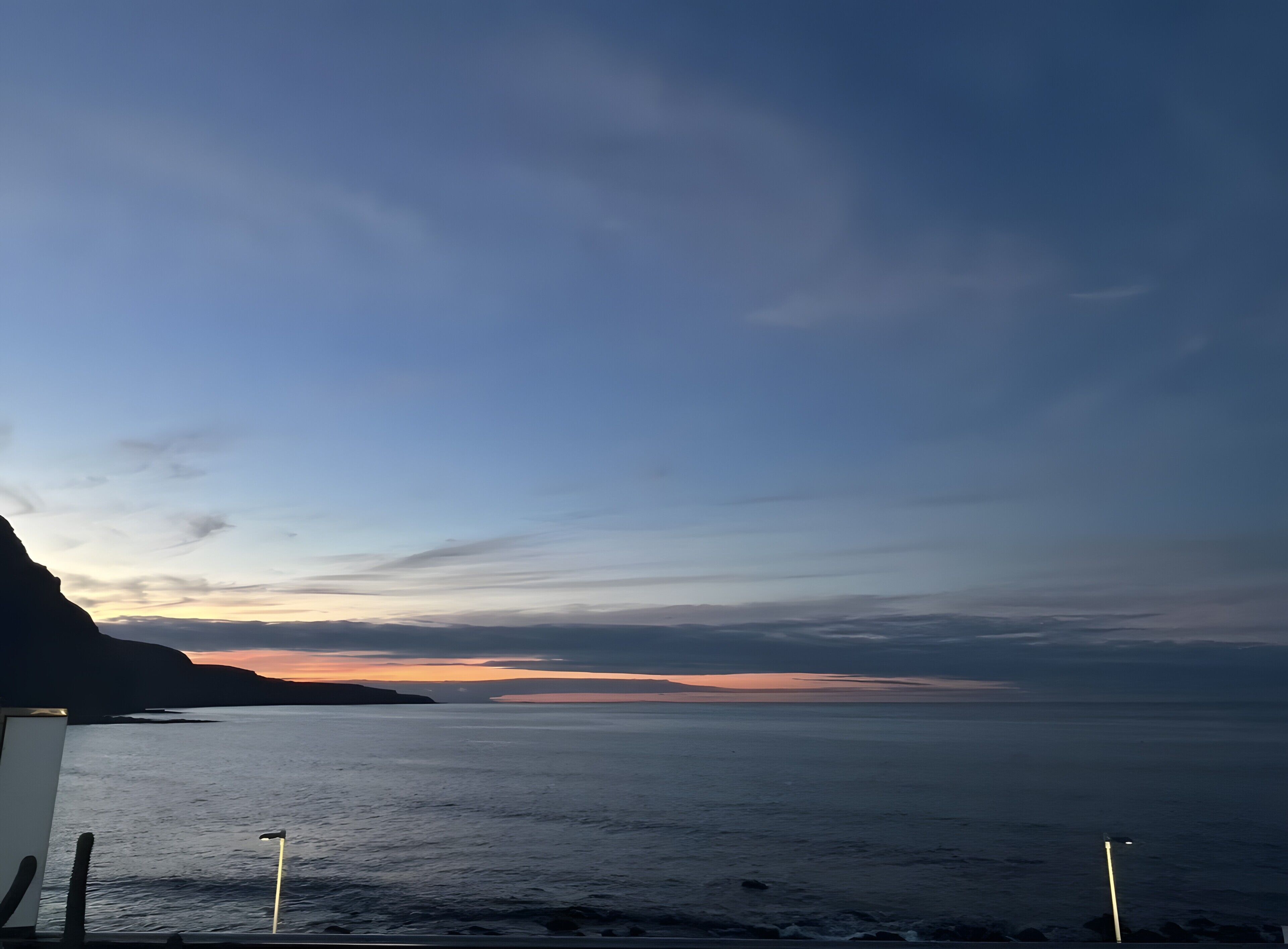 Vista costera con cielo despejado, mar tranquilo y un atardecer lejano.