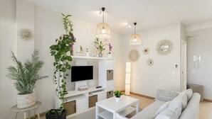 Una sala de estar moderna con televisor de pantalla plana, sofá blanco y plantas en macetas.