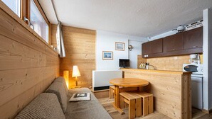 Een knus woongedeelte met houten inrichting, een bank, een eettafeltje, een televisie en een kitchenette.