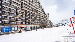Een hotel met meerdere verdiepingen en balkons, met een skipiste op de achtergrond en een bord voor 'INTERSPORT'.
