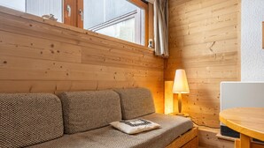 Een houten blokhut van binnen met een bank, een lamp en een eettafel.