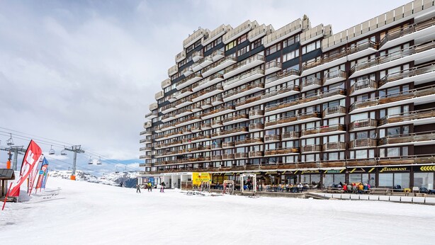 Een hotel met meerdere verdiepingen en balkons, met een skilift op de achtergrond en een met sneeuw bedekte grond.