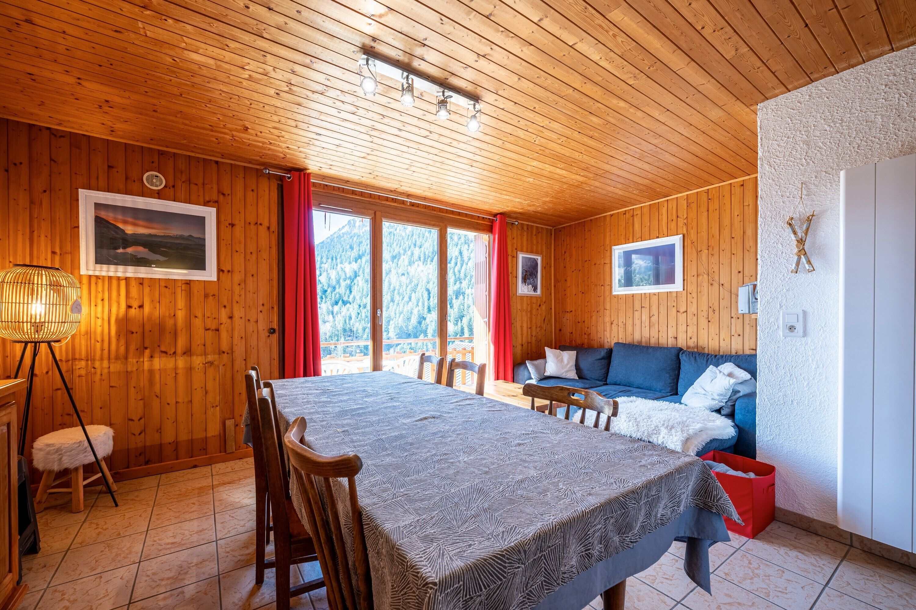 A wooden cabin interior with a dining table, chairs, a sofa, and a bed.