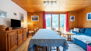 Une cabane en bois avec une table à manger, des chaises, un canapé, un téléviseur et des tableaux encadrés accrochés aux murs.