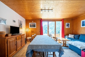 Une cabane en bois avec une table à manger, des chaises, un canapé, un téléviseur et des tableaux encadrés accrochés aux murs.
