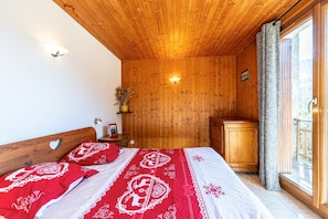 Une pièce aux murs lambrissés, comprenant un lit, une table de chevet, une lampe fixée au mur et une fenêtre avec des rideaux.