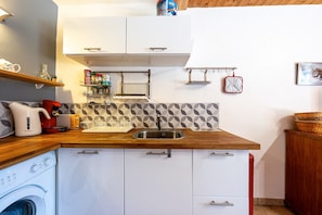 Une cuisine compacte équipée d’un lave-linge, d’une bouilloire, d’un évier et d’un plan de travail en bois.