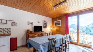 Un coin repas avec une table dressée pour quatre personnes, un téléviseur et une vue sur un paysage montagneux par le biais d’une grande fenêtre.